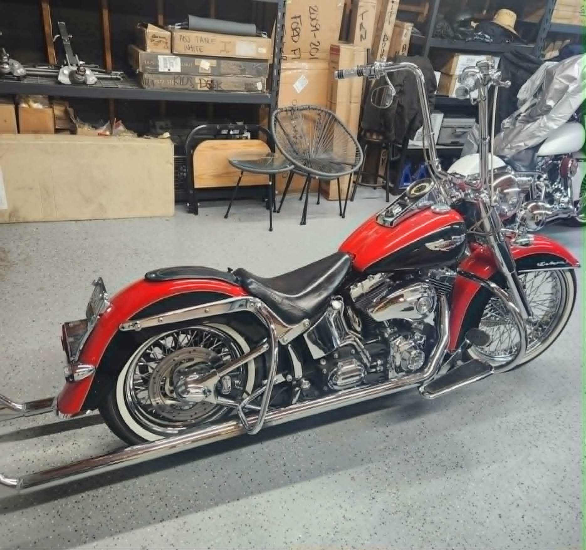 A red motorcycle parked on a vehicle transport trailer inside a storage garage with shelves holding boxes and various items in the background.