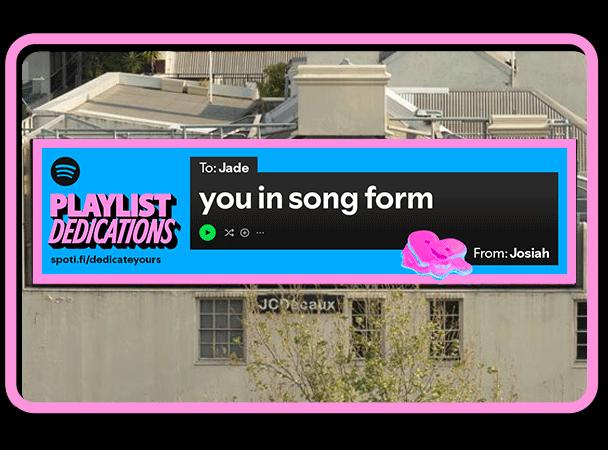 A digital billboard on a building displays a personalized Spotify playlist message from Josiah to Jade, with a pink border and a colorful graphic element.