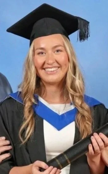 A young woman in graduation cap and gown, smiling while holding a diploma.
