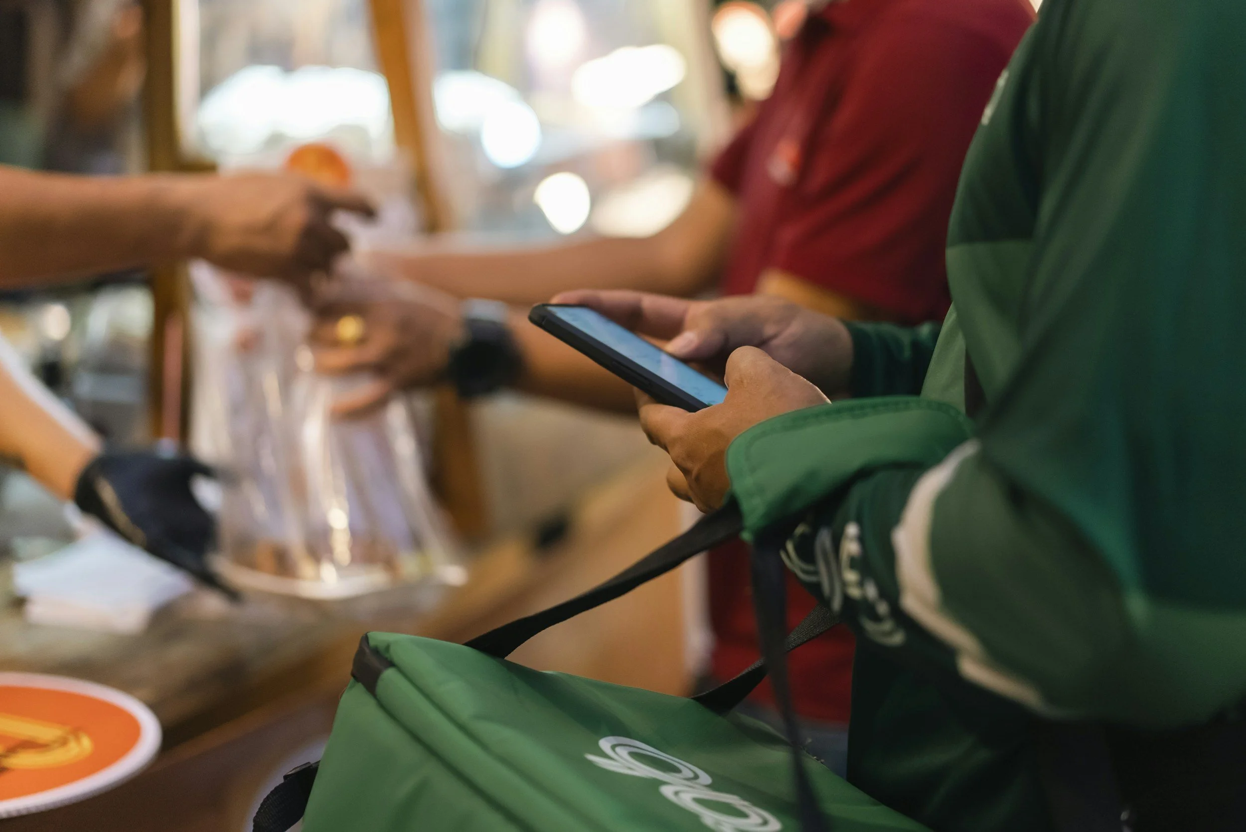 People seated at a counter, with one person using a smartphone, in what appears to be a casual setting like a cafe or restaurant.