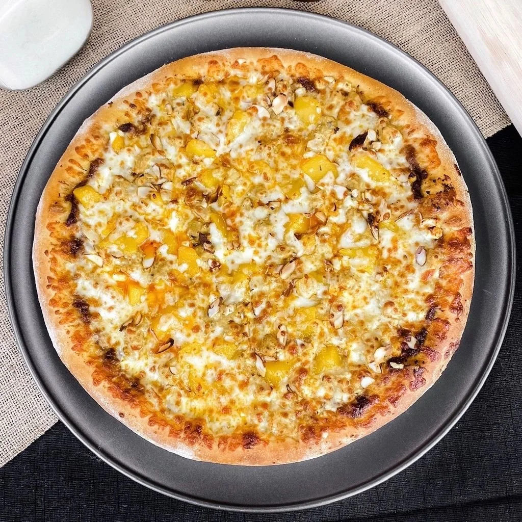 Cheese pizza topped with pineapple chunks and chopped nuts on a dark pizza tray.