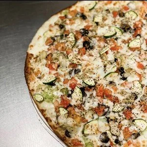 A pizza topped with various vegetables such as zucchini, tomatoes, and black olives, with melted cheese.