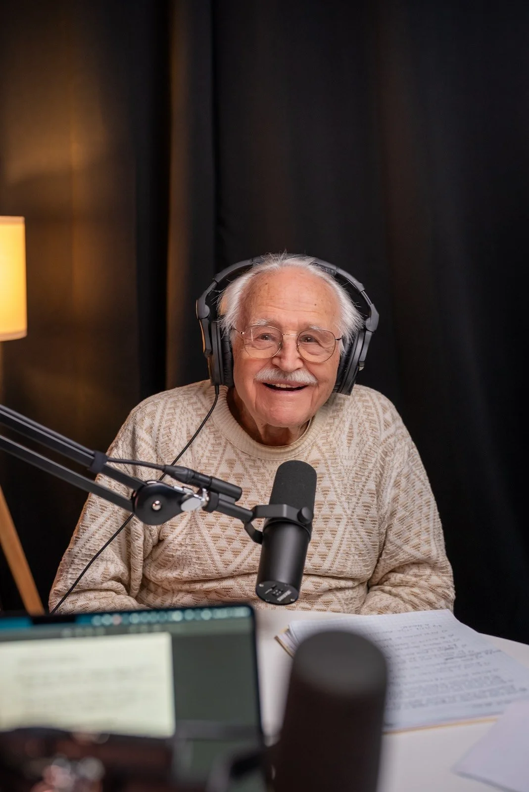 A smiling older man wearing headphones and recording a podcast at Noble Frequency studio in Temecula–Murrieta.