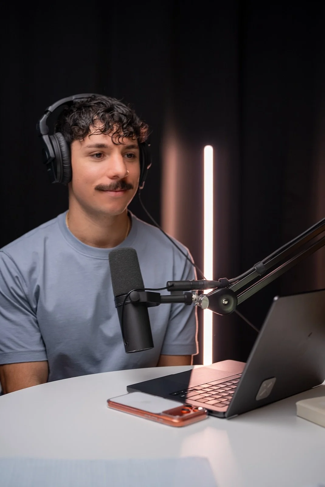 A man in headphones recording a podcast at his mic and laptop at Noble Frequency studio in Temecula–Murrieta.