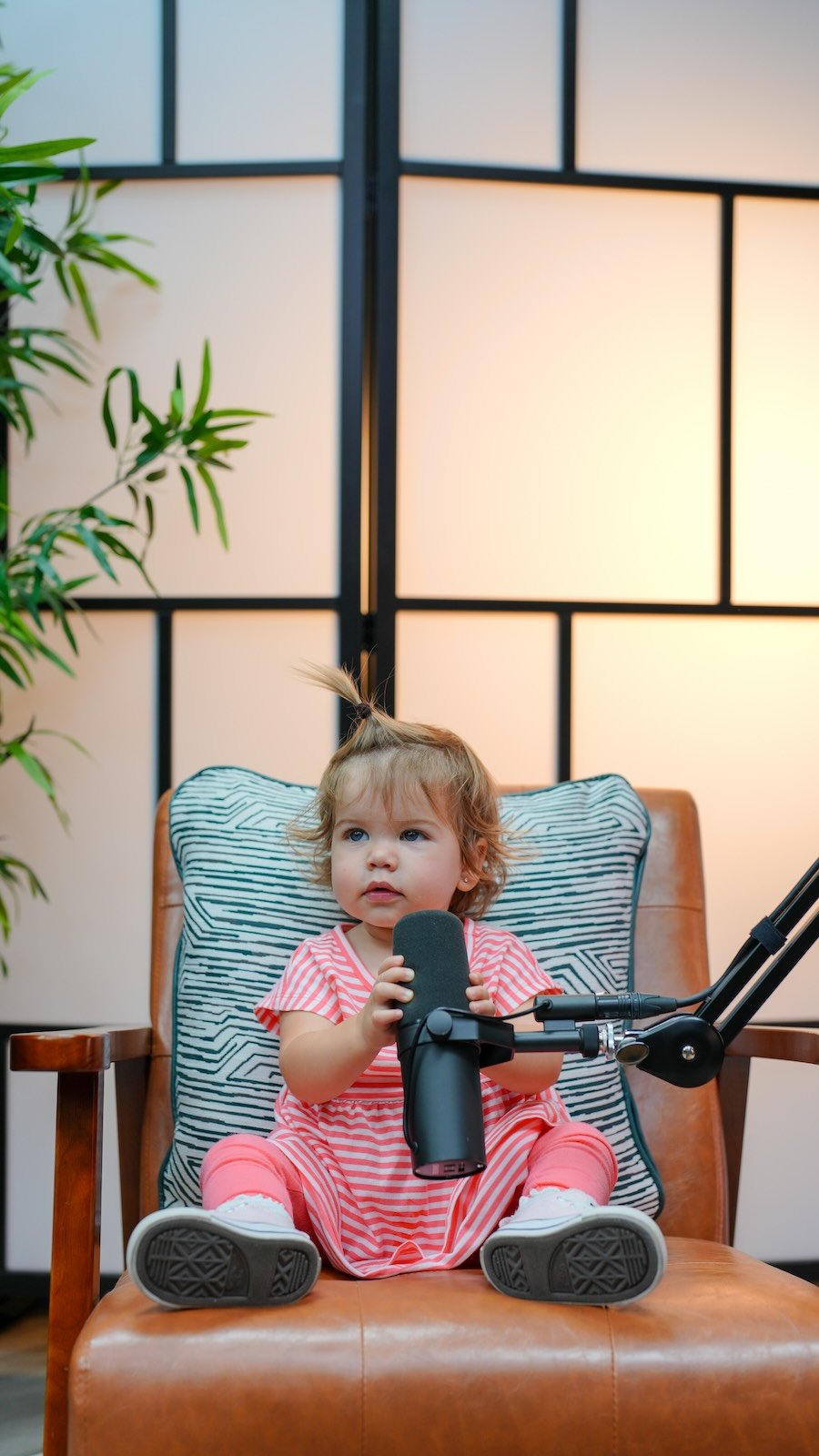 A toddler sitting in the studio chair holding a podcast mic at Noble Frequency in Temecula–Murrieta.