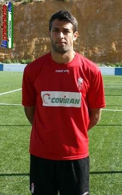 A young man in a red soccer jersey standing outdoors on a soccer field.