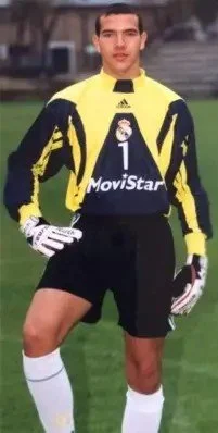 A young male soccer goalkeeper standing on a field in a yellow and black goalkeeper uniform, with black shorts, white socks, and gloves.