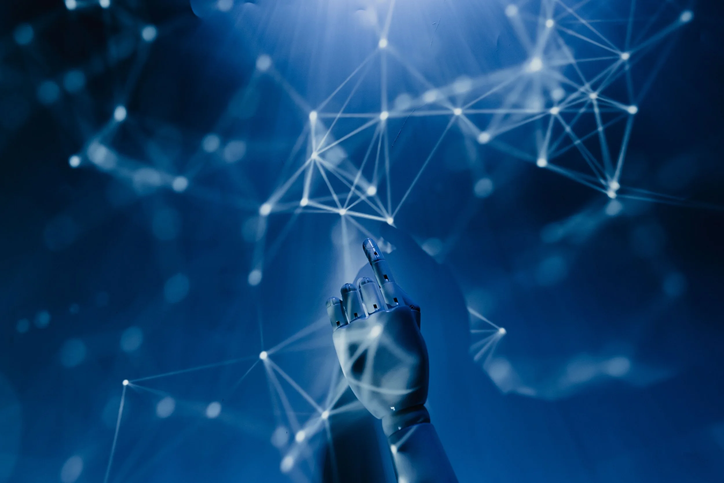 Una mano robótica apunta hacia un fondo azul con conexiones de luz, representando tecnología y redes digitales.