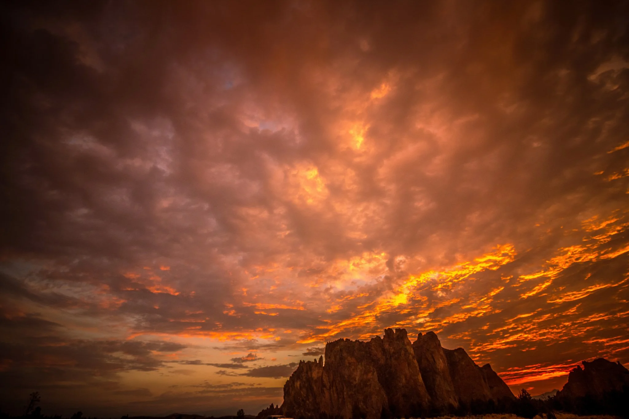 Sunset with dark clouds and orange hues over rocky cliffs.