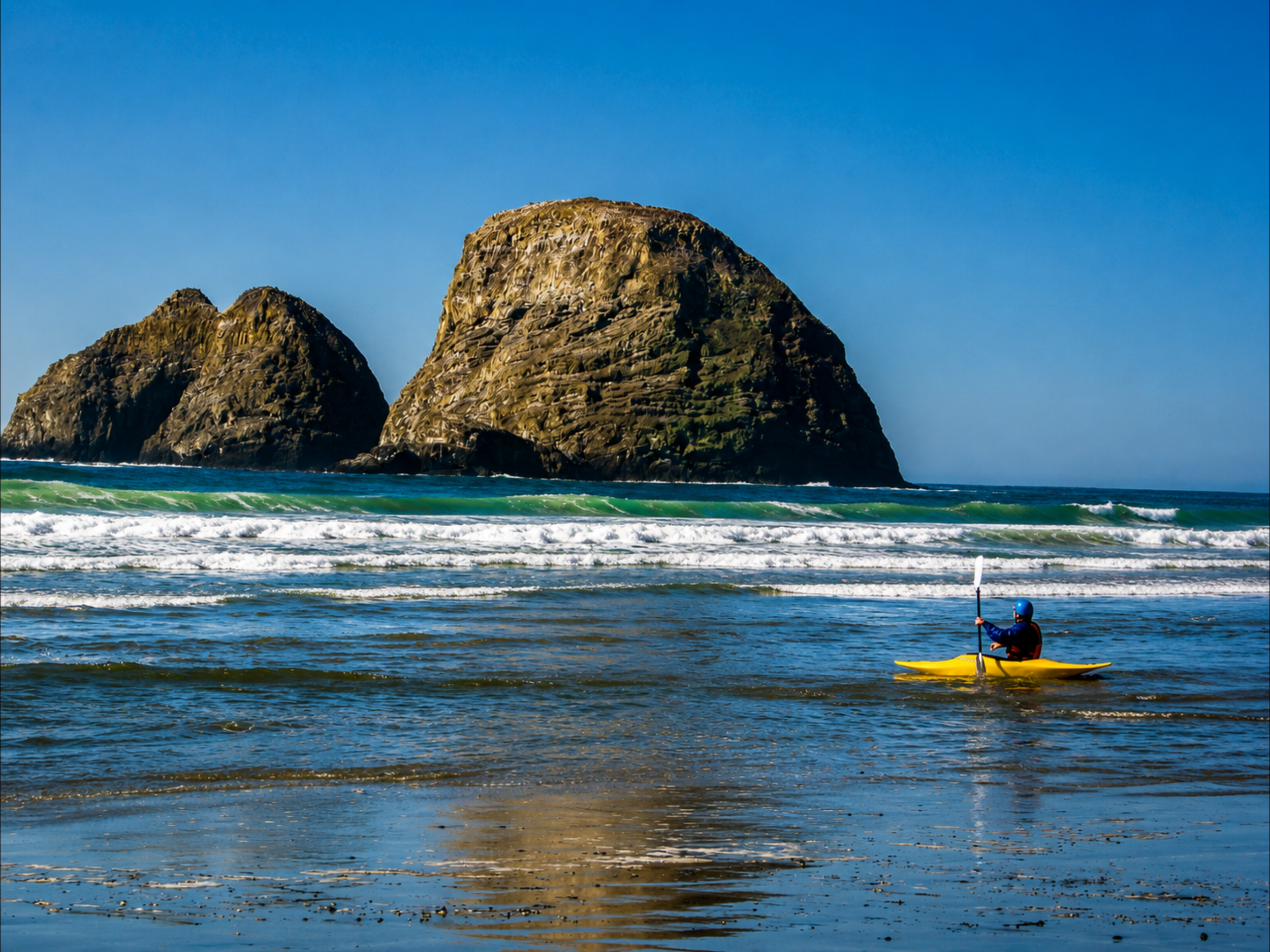 A person kayaking in the ocean near large rocky islands with blue sky above.