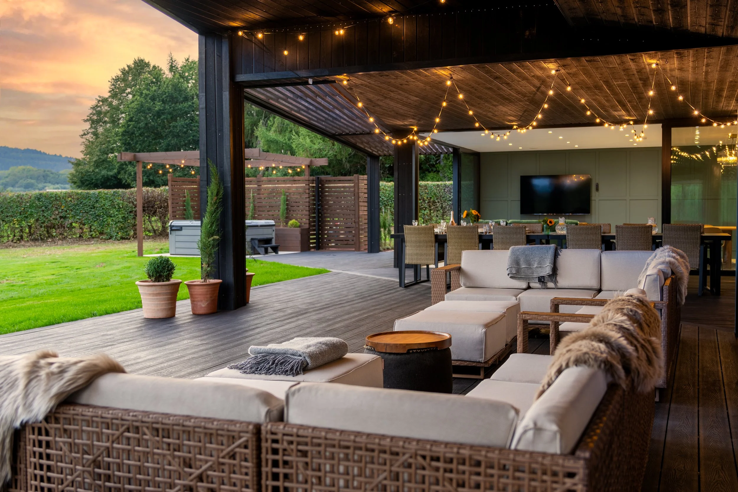 Outdoor patio with furniture, string lights, and a view of the backyard with green grass and trees at sunset.