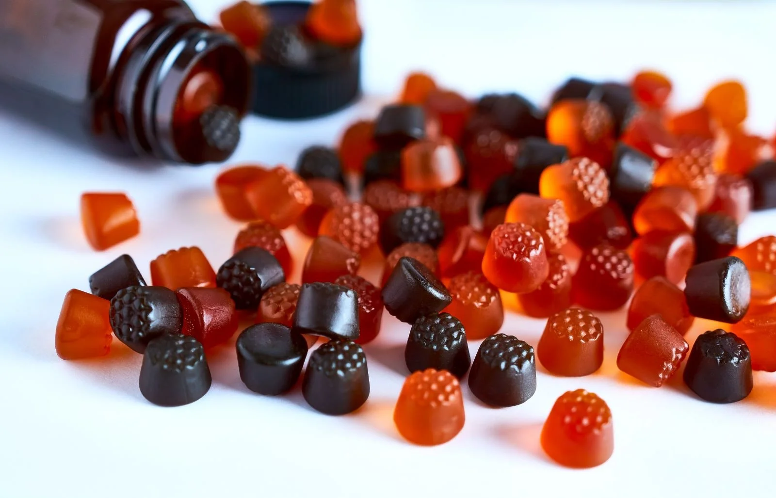 Assorted black and orange gummy candies spilled from a brown bottle onto a white surface.