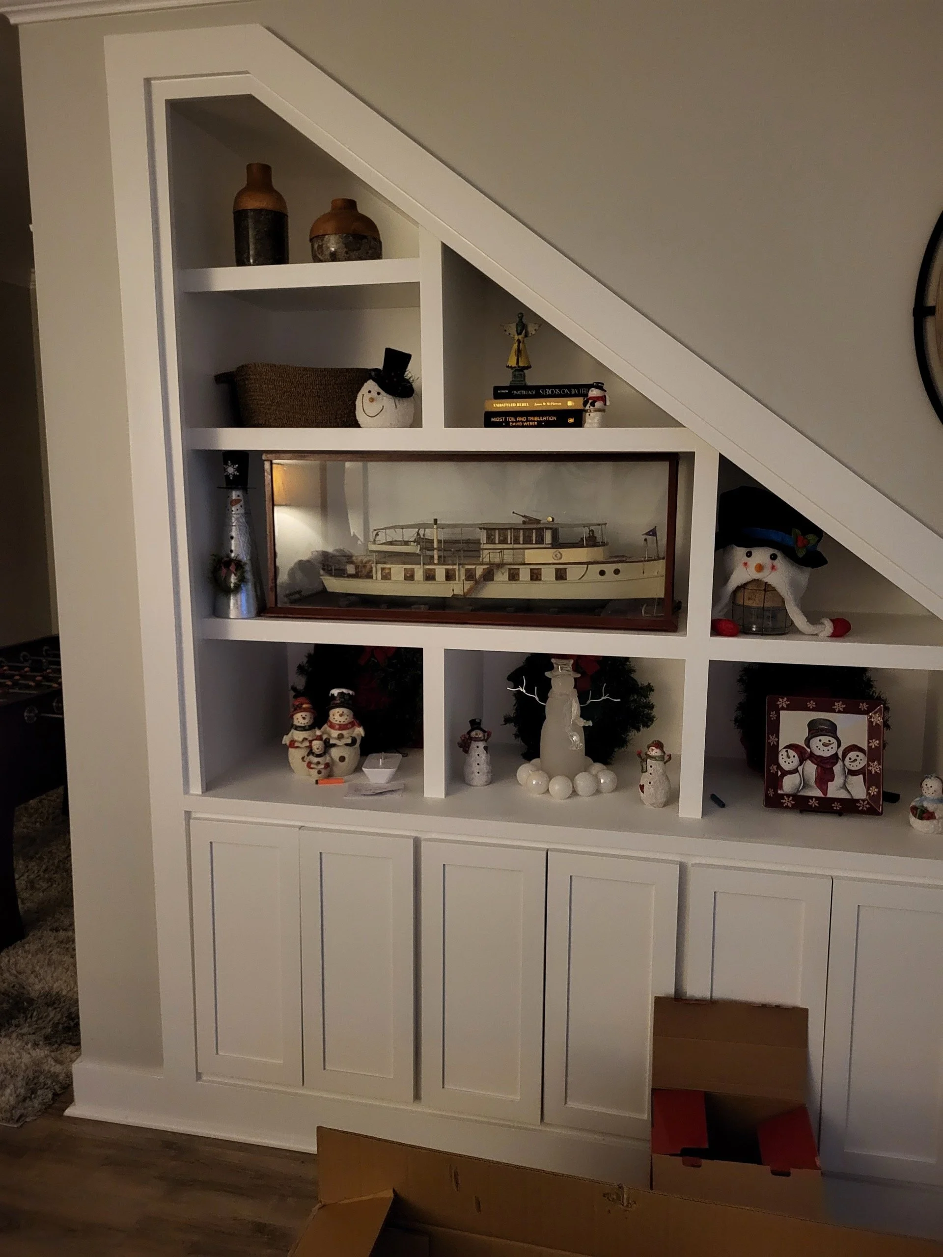 White bookshelf decorated with holiday and nautical items, including snowmen, a model boat, and houseplants.