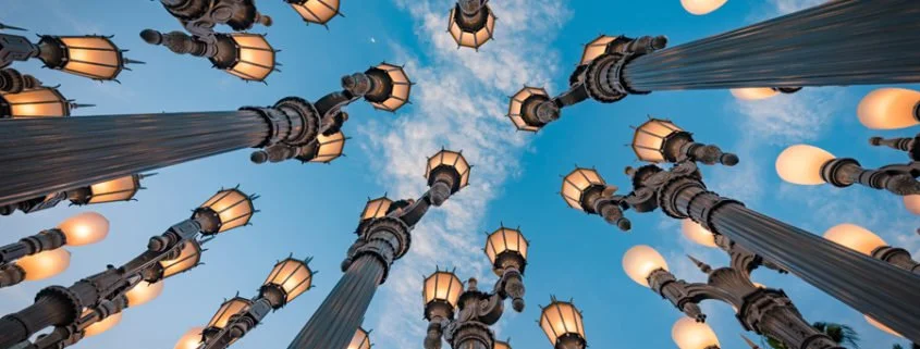 LACMA: Looking up at tall vintage street lamps against a blue sky with clouds.