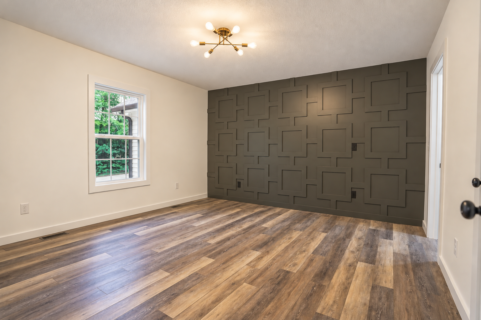 Empty room with wood flooring and a dark gray paneled accent wall.