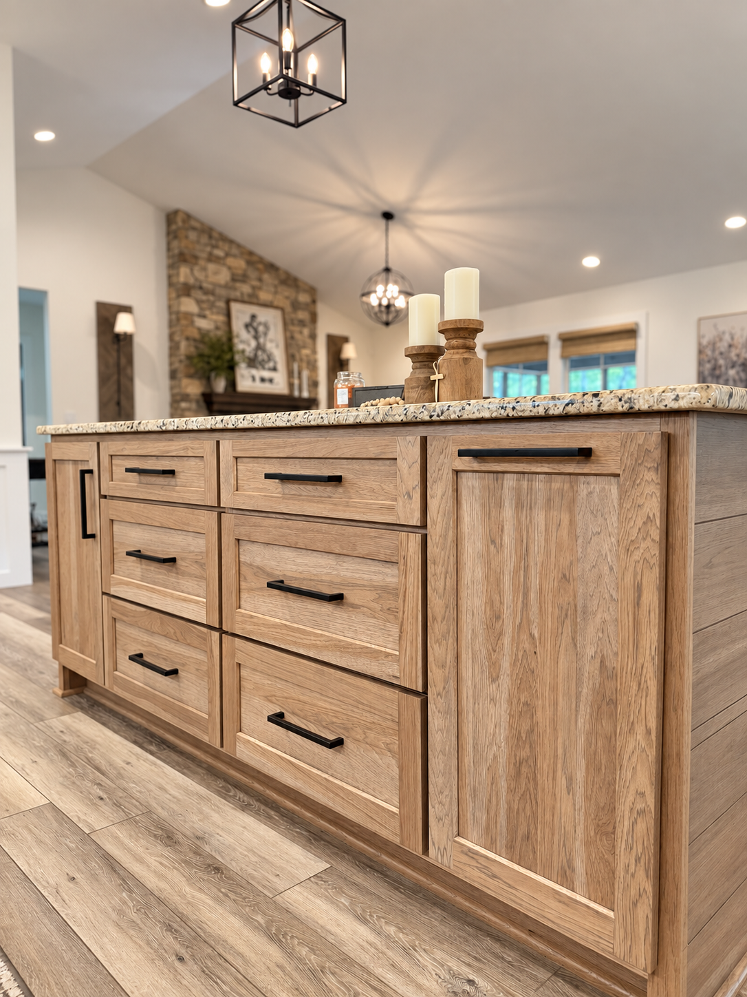 Wood kitchen island with drawers and black handles beneath pendant lights.