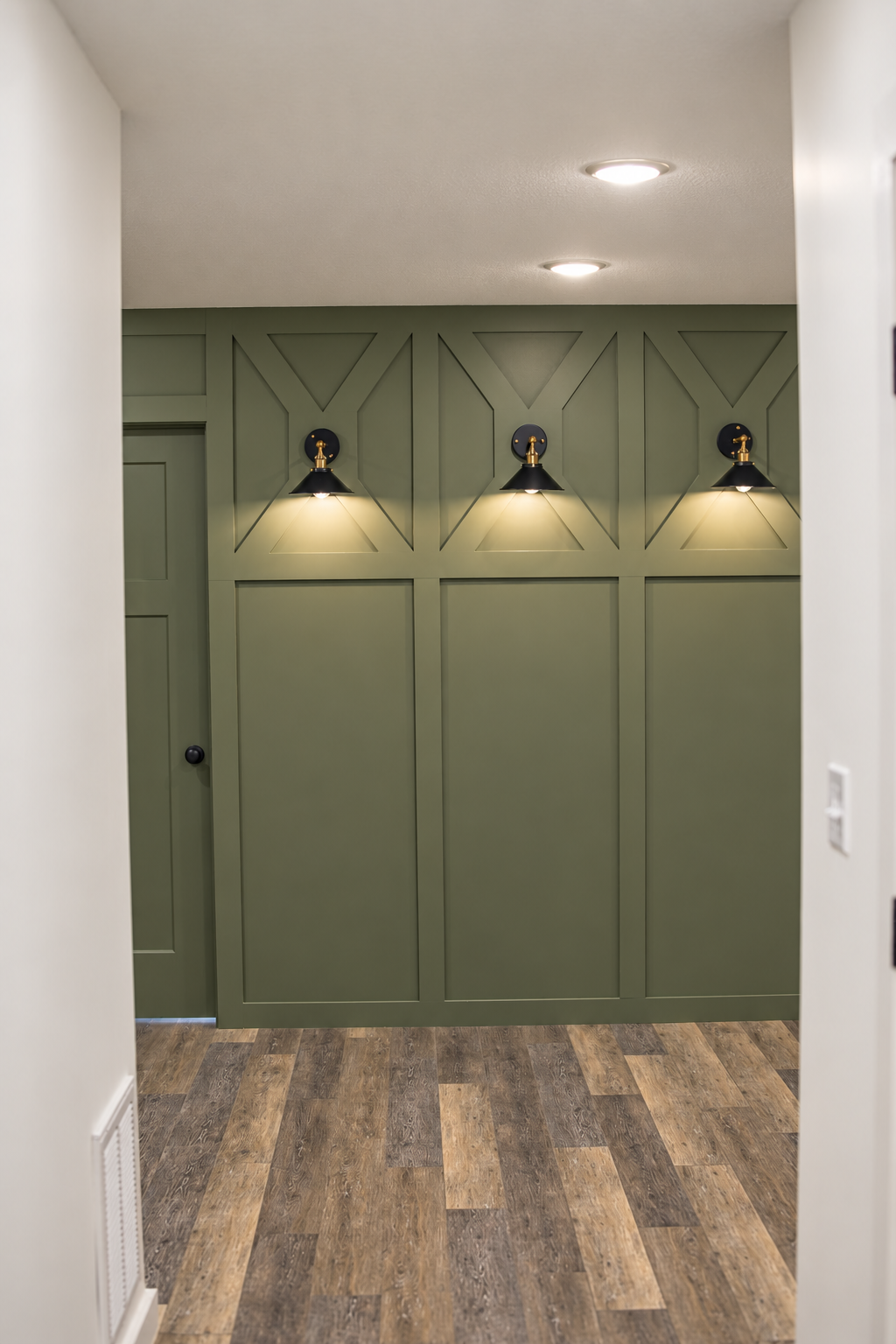Green paneled accent wall with three black wall sconces.
