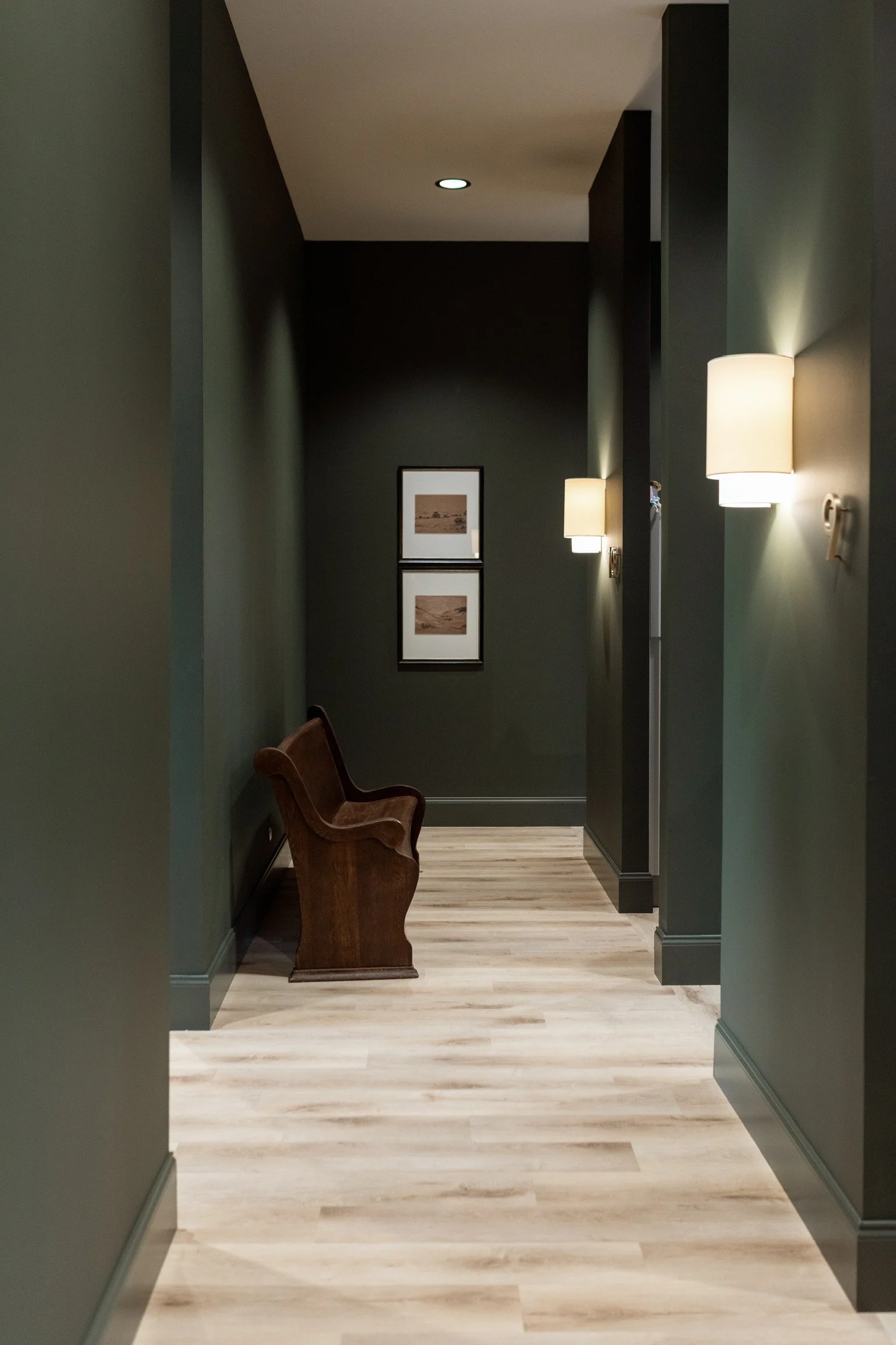 Hallway with green walls, wood flooring, and framed landscape art.