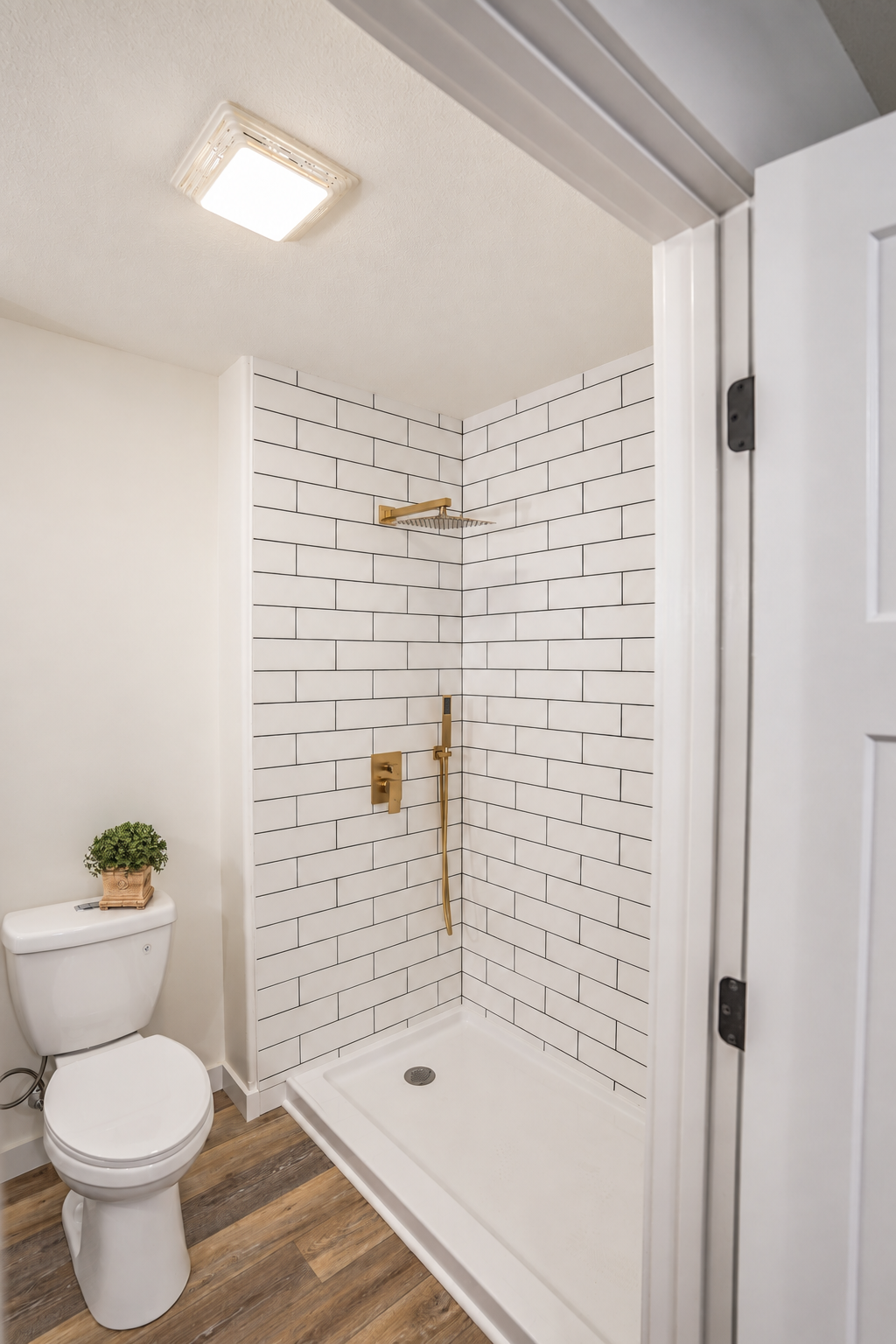 White tiled shower with gold fixtures beside a toilet.