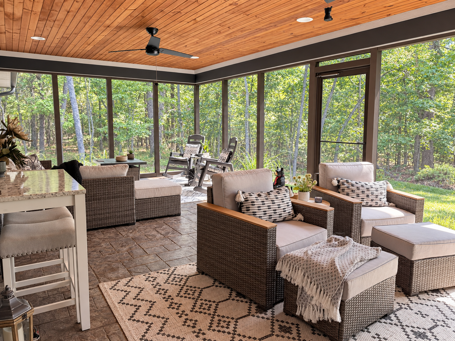 Covered porch with wicker seating, a patterned rug, and a view of the wooded yard.