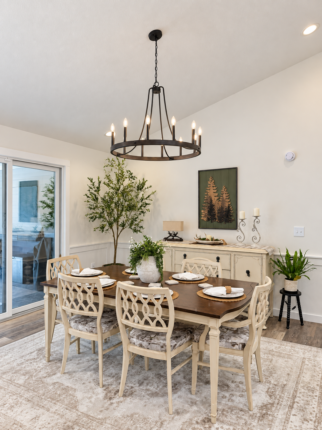 Dining room with a wooden table, six cream chairs, a chandelier, a sideboard, plants, and wall art.