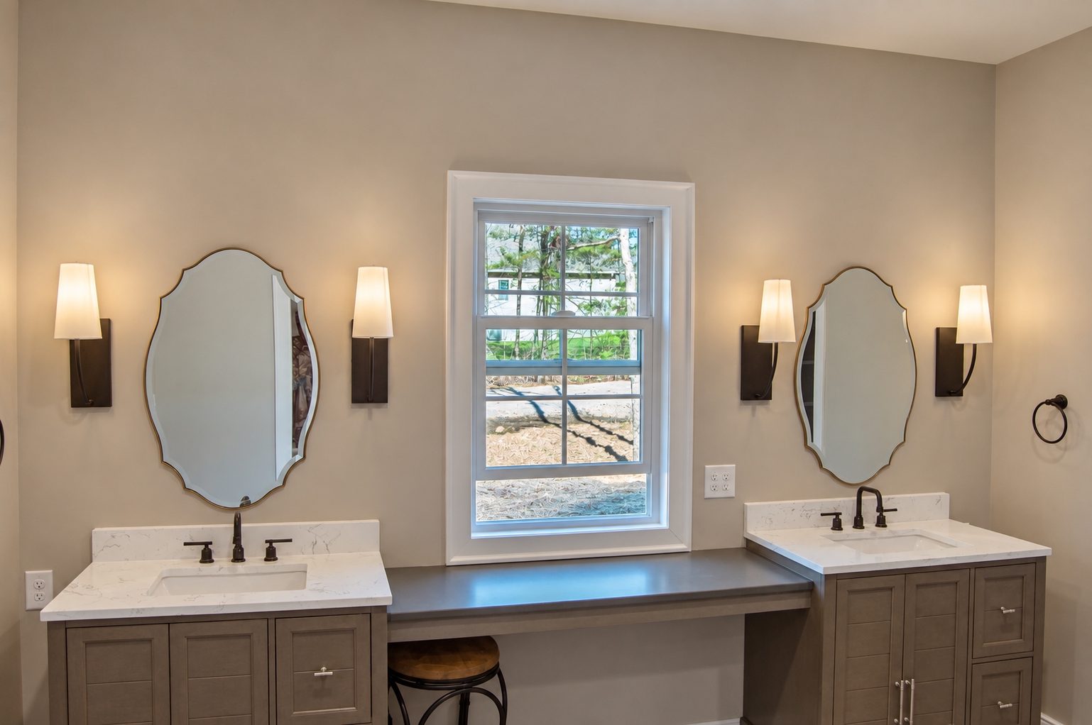 Bathroom with two vanities, round mirrors, wall lights, and a window between the sinks.