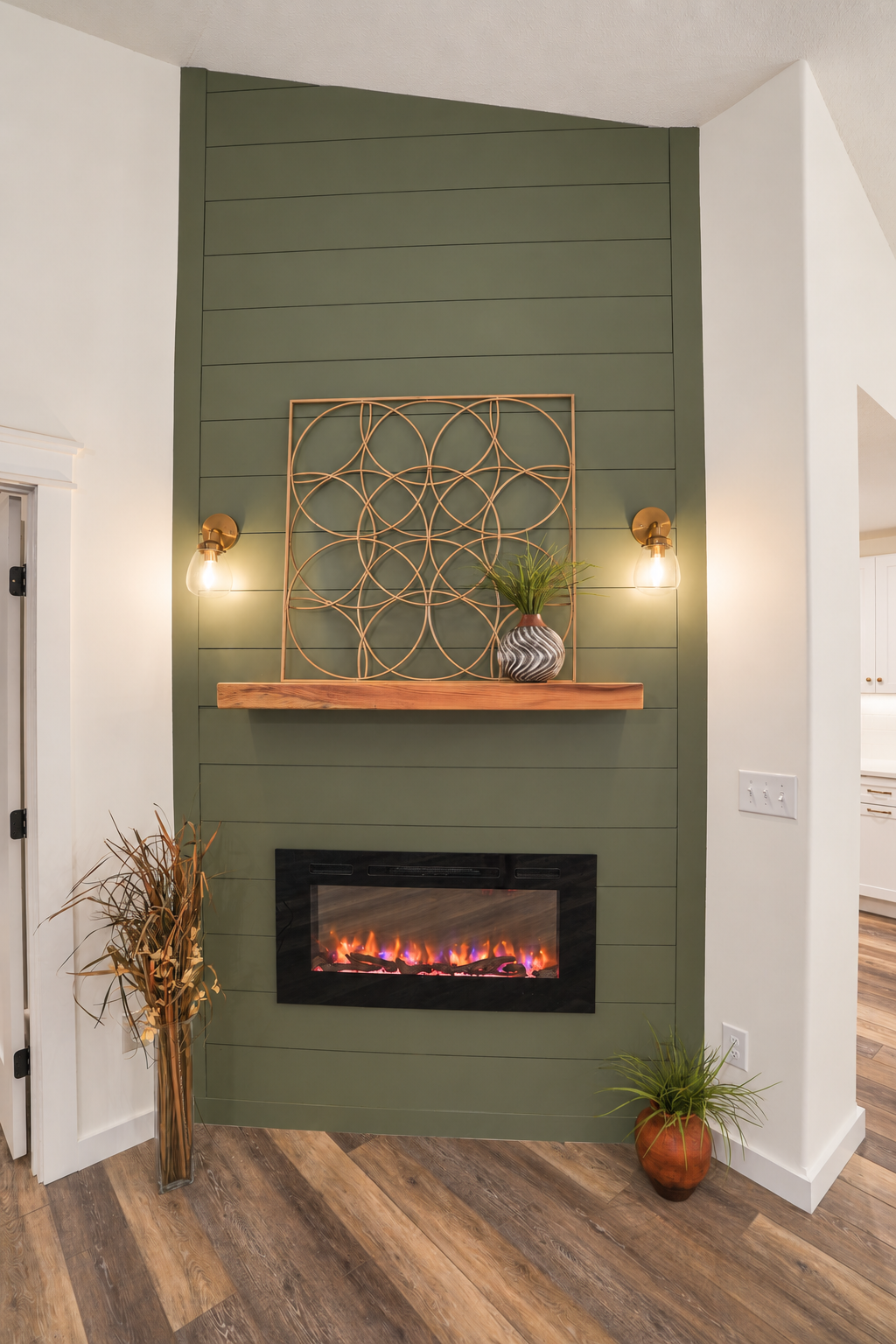 Fireplace set into a green accent wall with a wood mantel and wall lights.