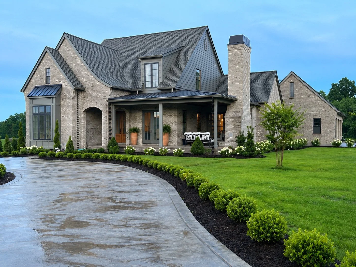 Large brick and siding home with a covered porch and curved driveway.