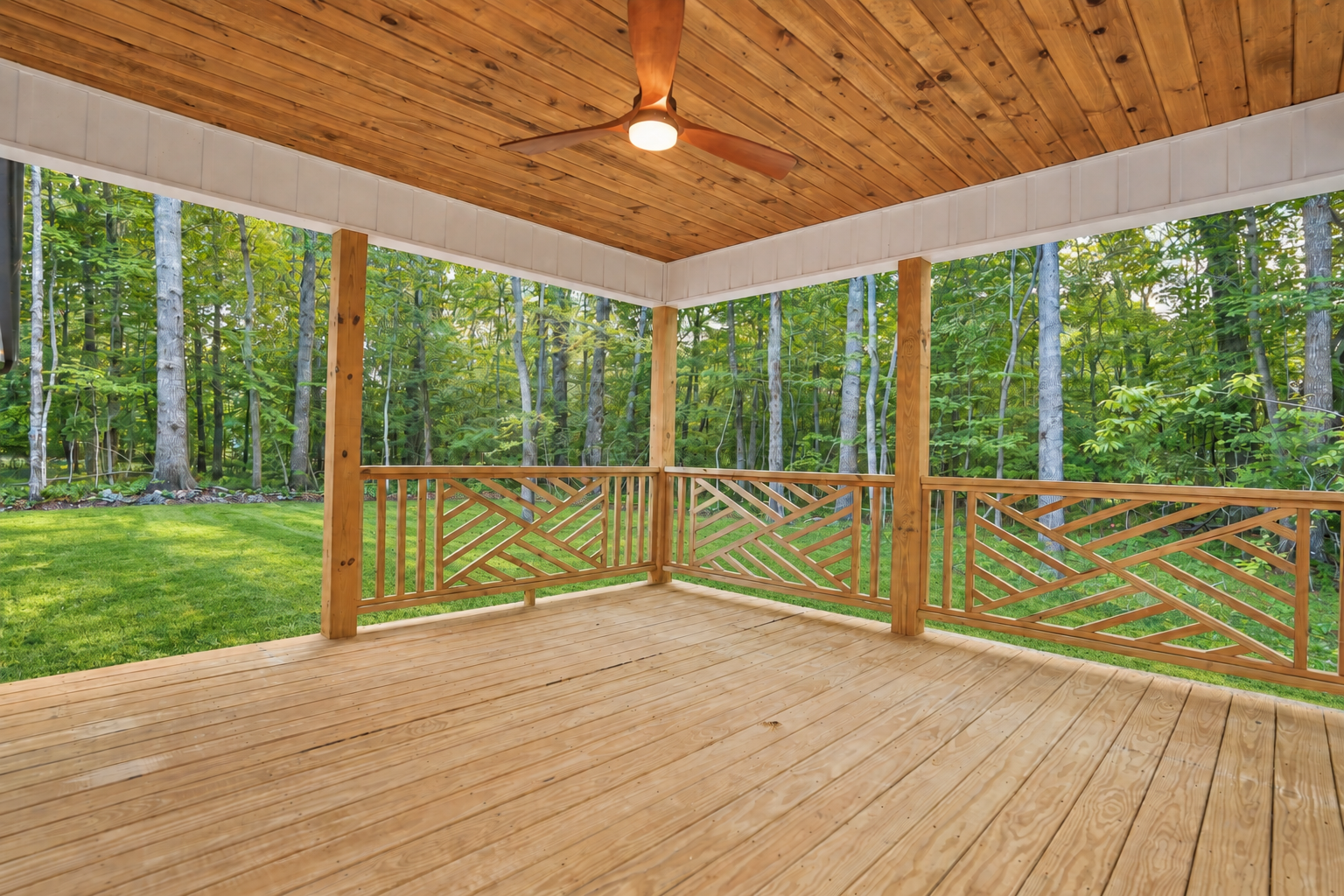 Covered wood porch with a ceiling fan overlooking trees.