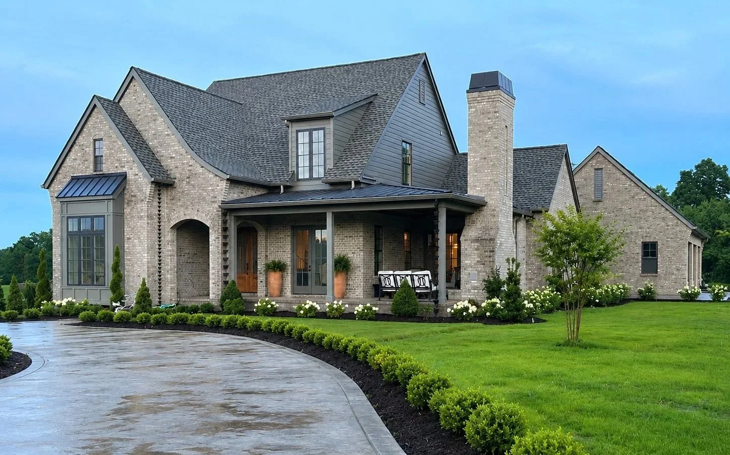 A large brick home with multiple gables, a covered front entry, and a curved driveway. 