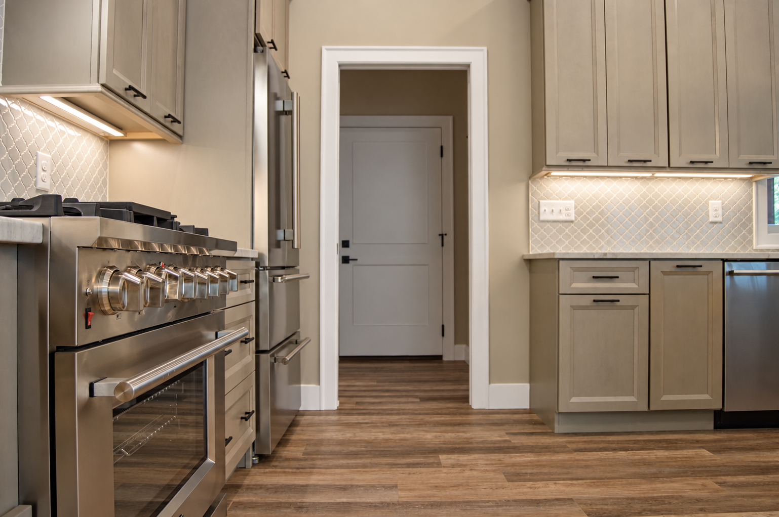 Modern kitchen with stainless steel appliances, beige cabinets, and wood flooring.