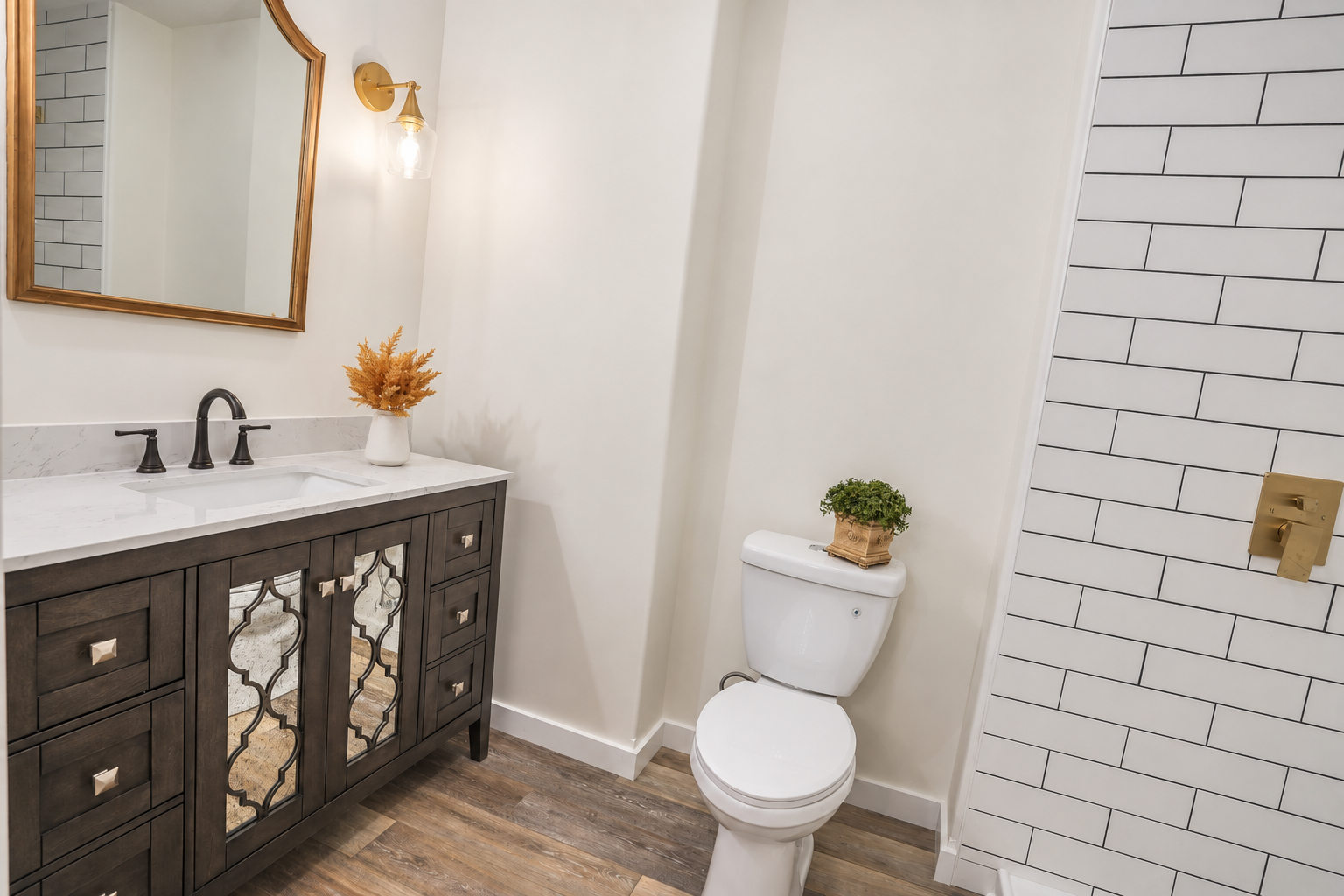 Bathroom with a dark wood vanity, gold-framed mirror, and white subway tile.
