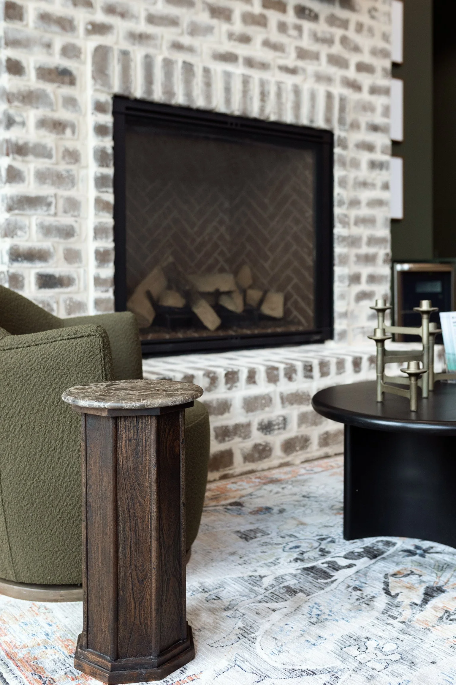 Commercial office waiting room with a brick fireplace, green armchair, and a patterned rug.