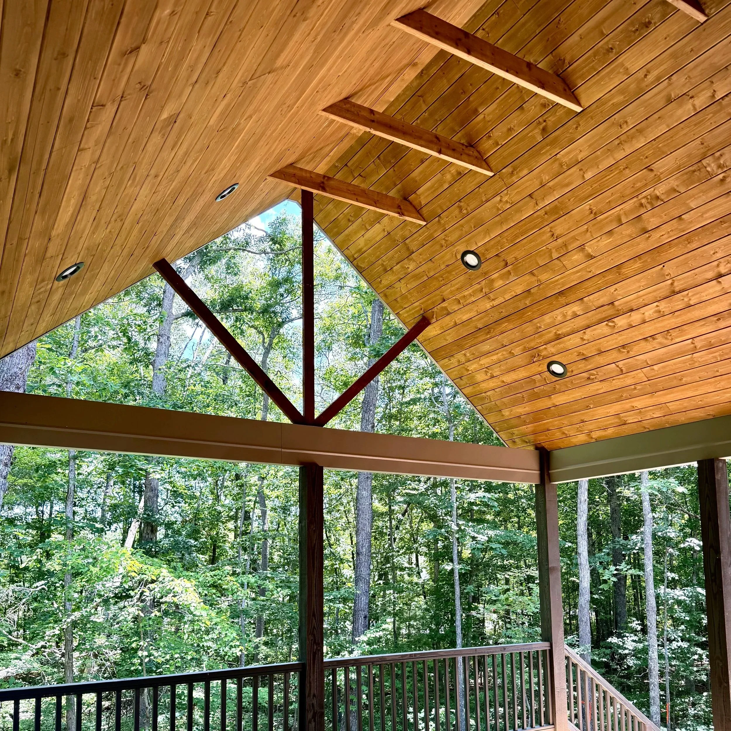 The image shows a wooden ceiling with skylights and spotlights, with trees visible outside through the open ceiling design.