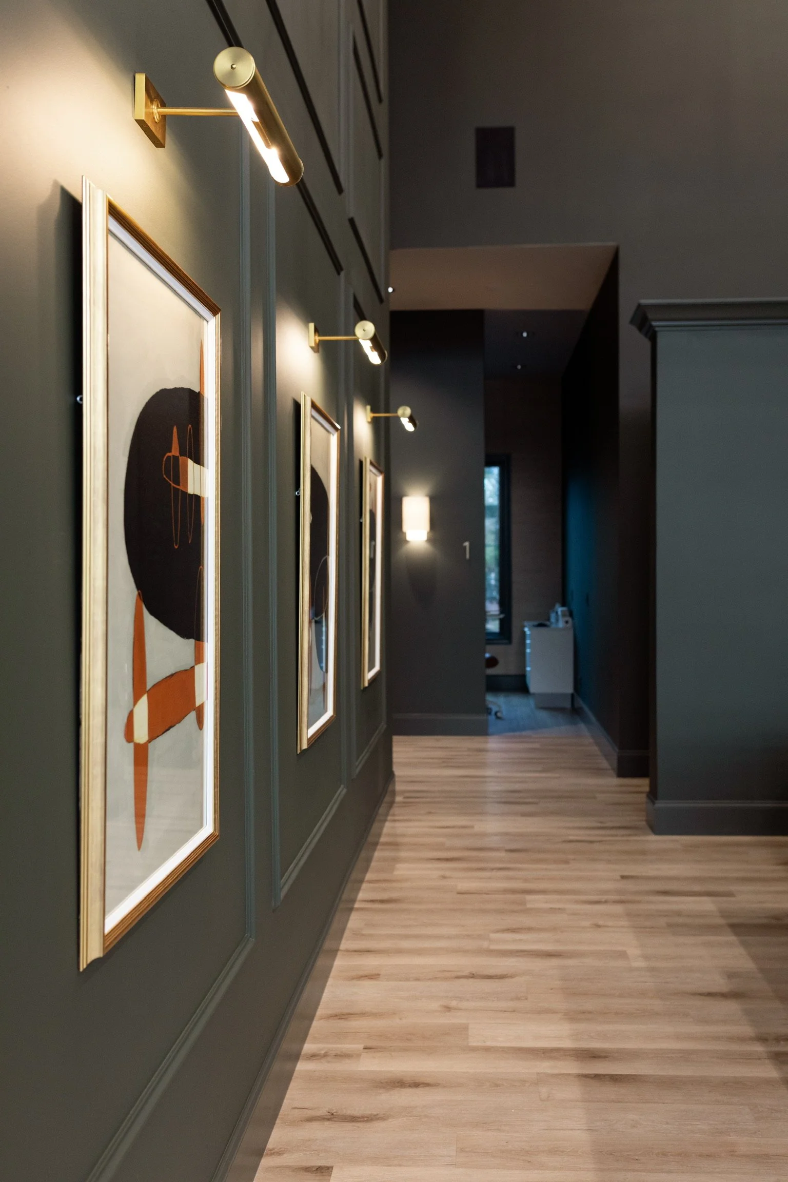 Hallway with dark green walls, framed artwork, and wood flooring. 