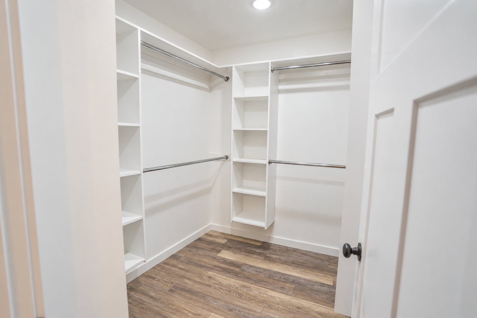 Walk-in closet with white built-in shelves and clothing rods.