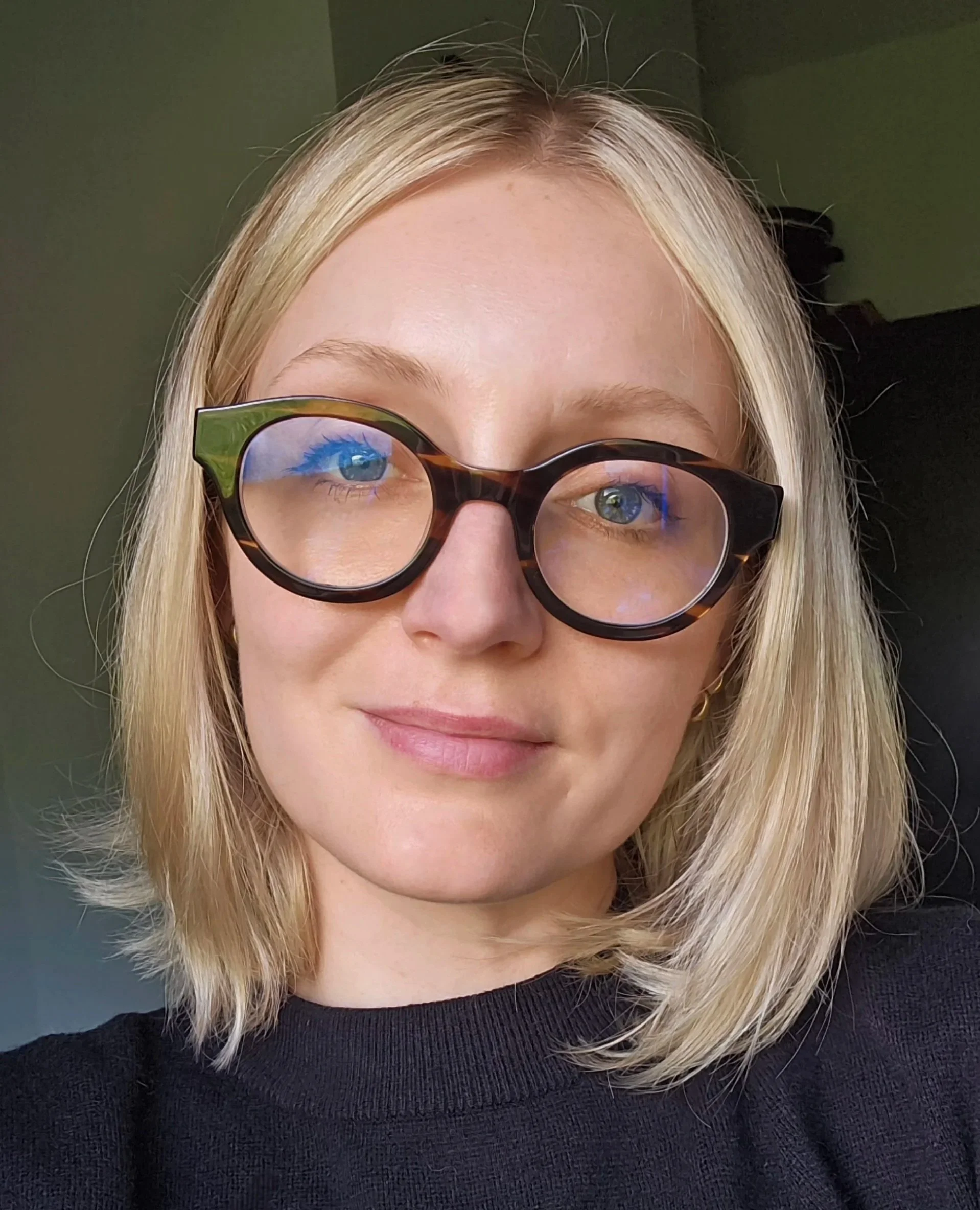 Close-up of a woman with blonde hair wearing black and tortoiseshell glasses and a black top.