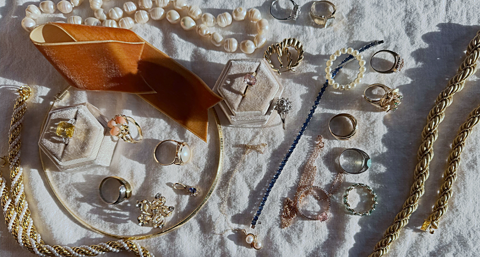 Rings, necklaces, bracelets and earrings arranged on fabric with jewelry boxes and display trays.