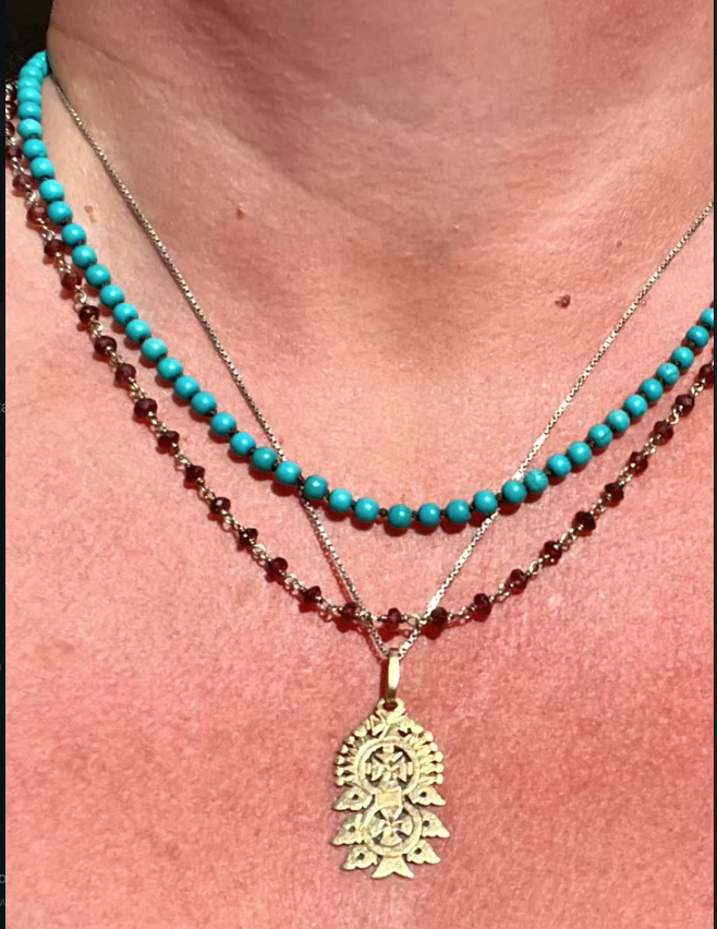 Close-up of a turquoise beaded necklace layered with other necklaces