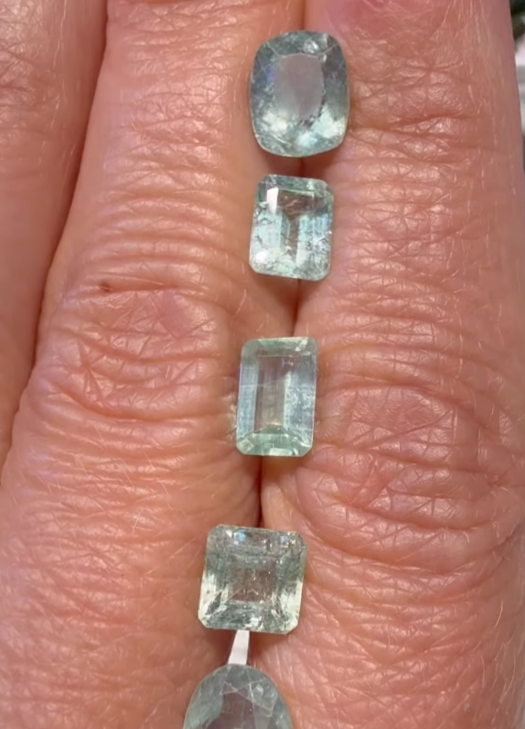 Light blue loose gemstones lined up on a finger.