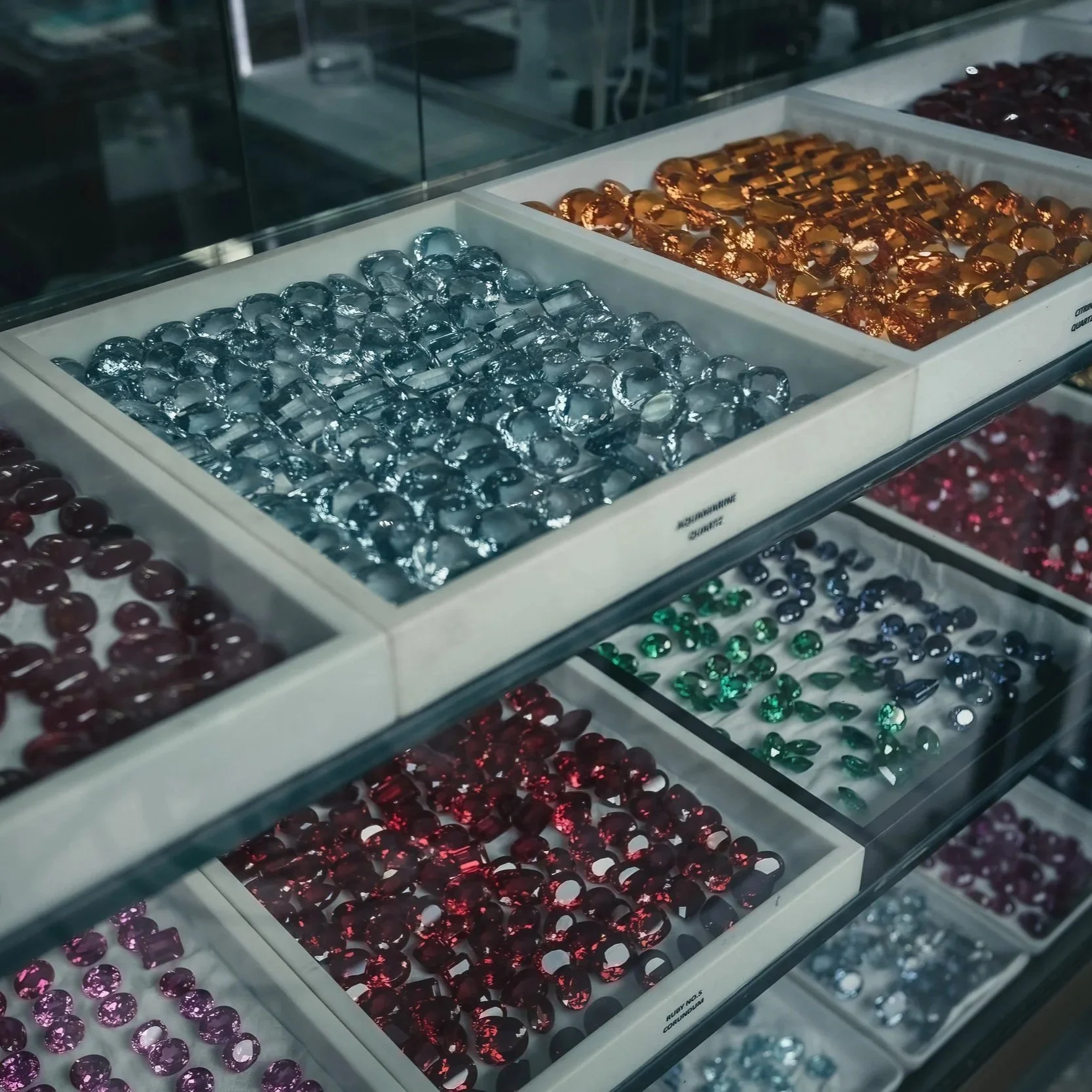 Colorful loose stones arranged in trays at a jewelry counter.