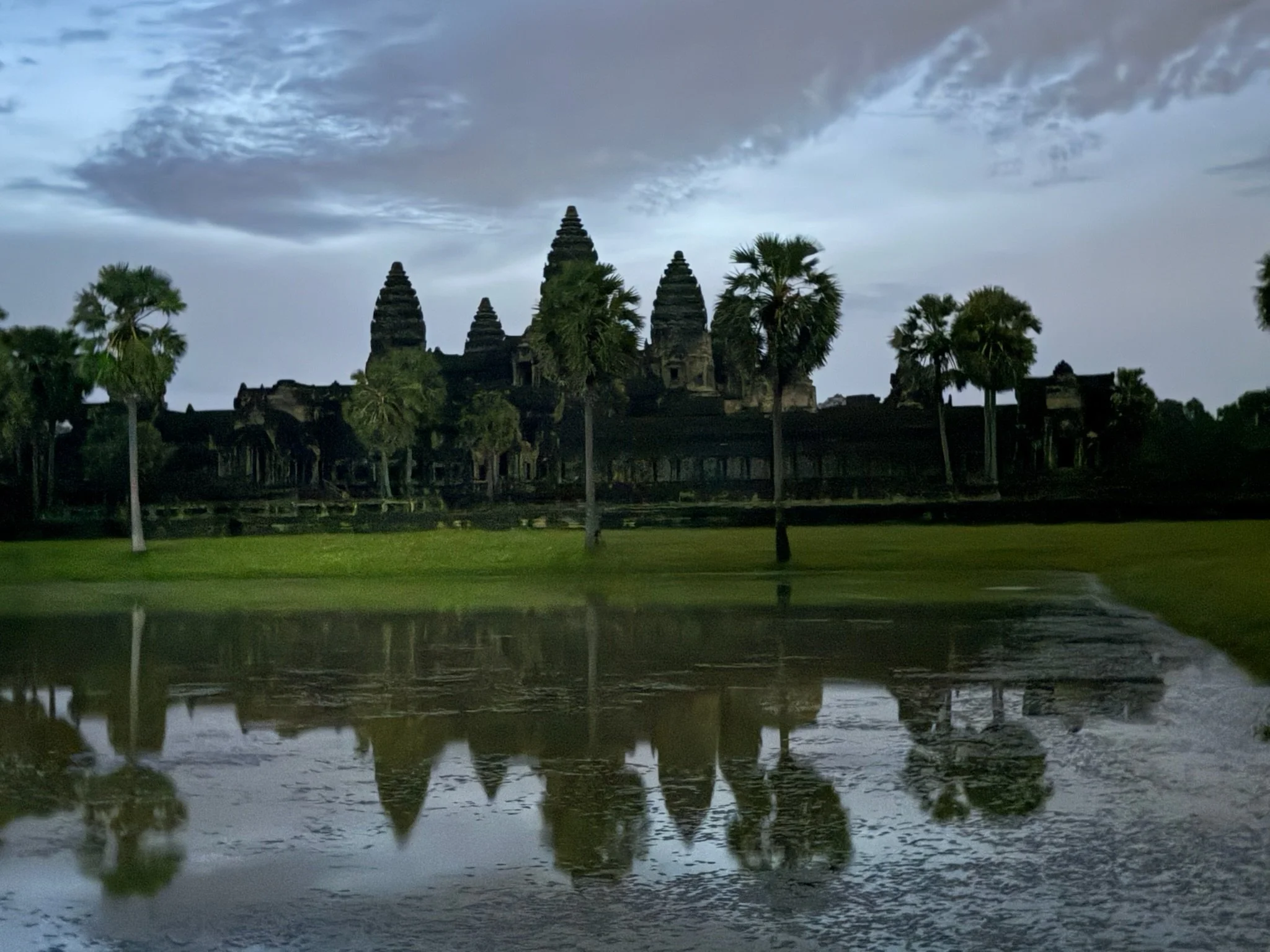 Temple towers and palm trees reflected in a pond.