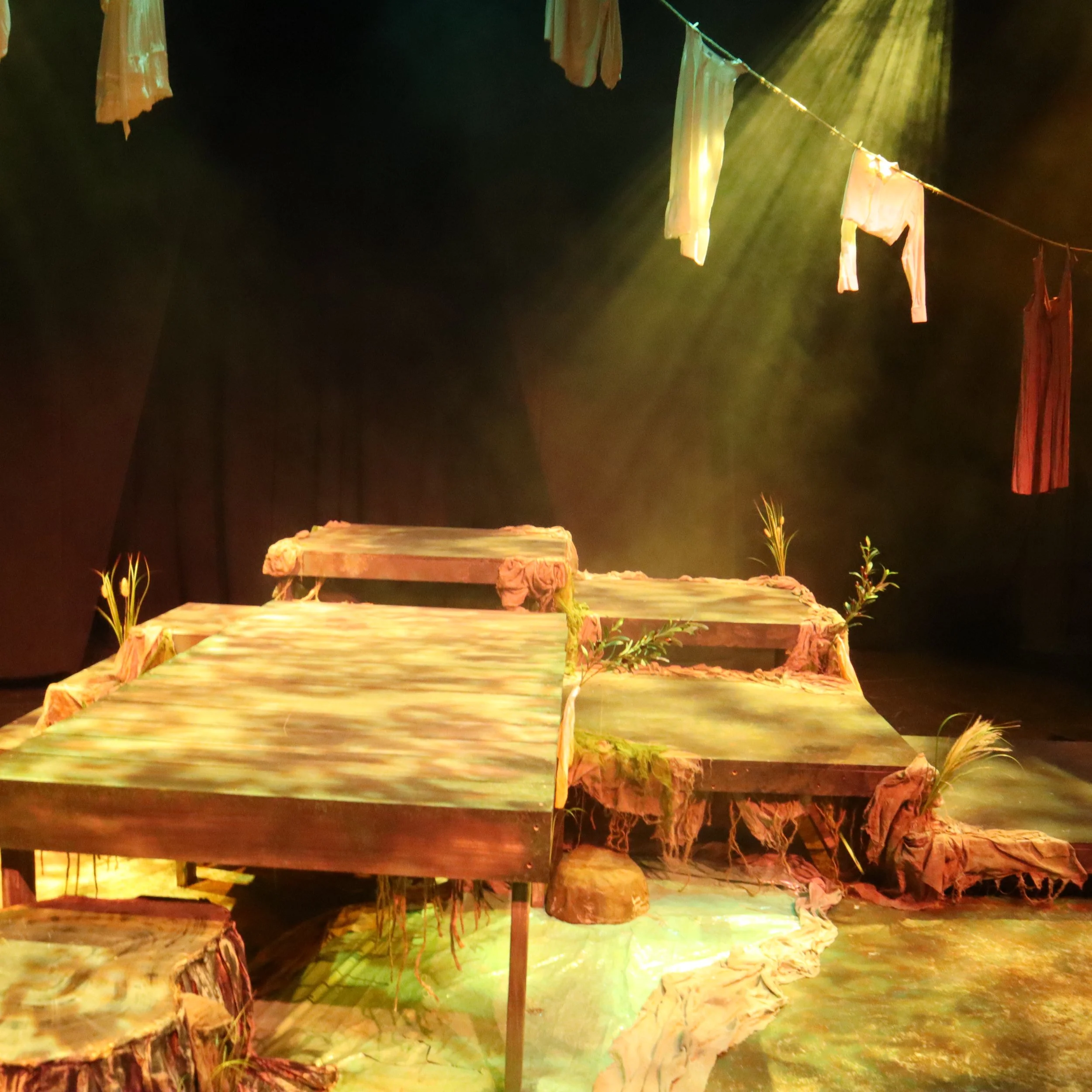 Colorful fabric or paper hanging on a clothesline, illuminated by stage or spotlights, with a dark background.