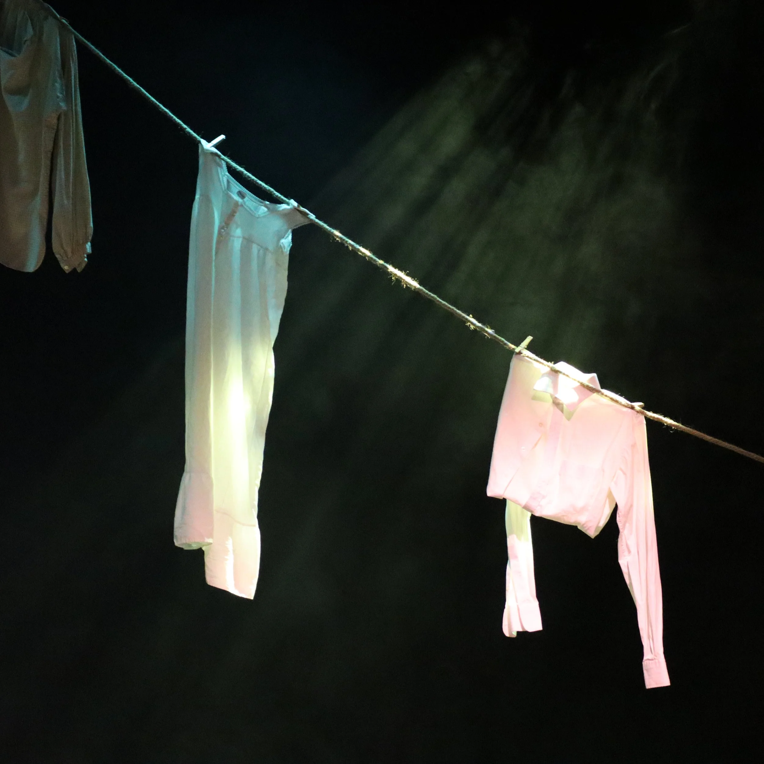Laundry drying on a clothesline at night with flashlights illuminating the hanging clothes, including shirts and pants, against a dark sky.