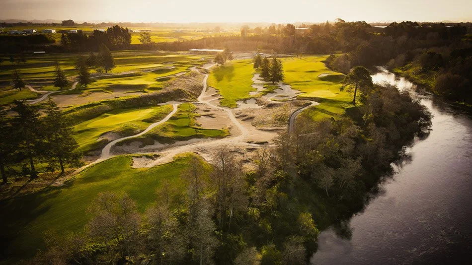 Aerial view of a golf course with sand traps and green fairways, next to a winding river surrounded by trees. Tieke Golf Estate with Kiwi Golf Adventures