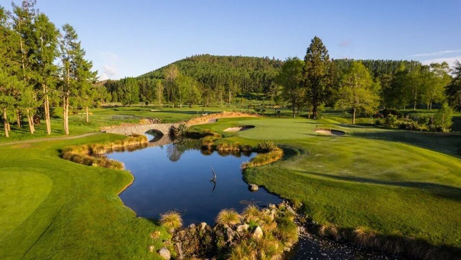 A scenic golf course with a pond, trees, bunkers, and a mountain in the background under a clear blue sky. Wairakei Golf Sanctuary