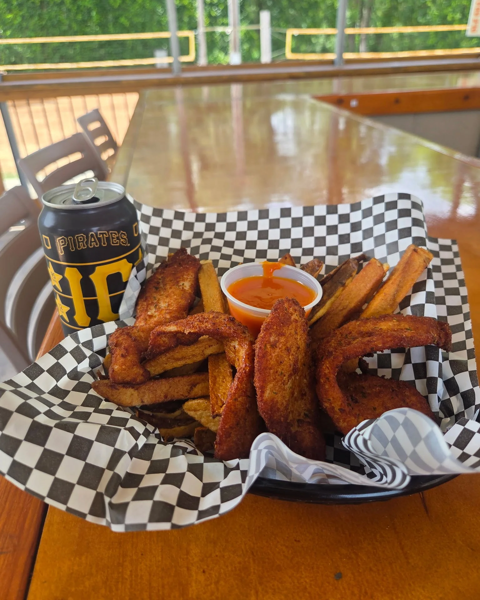 Basket of fried chicken wings, potato wedges, and a small cup of dipping sauce, with a can of Pepsi, on a checkered paper liner.