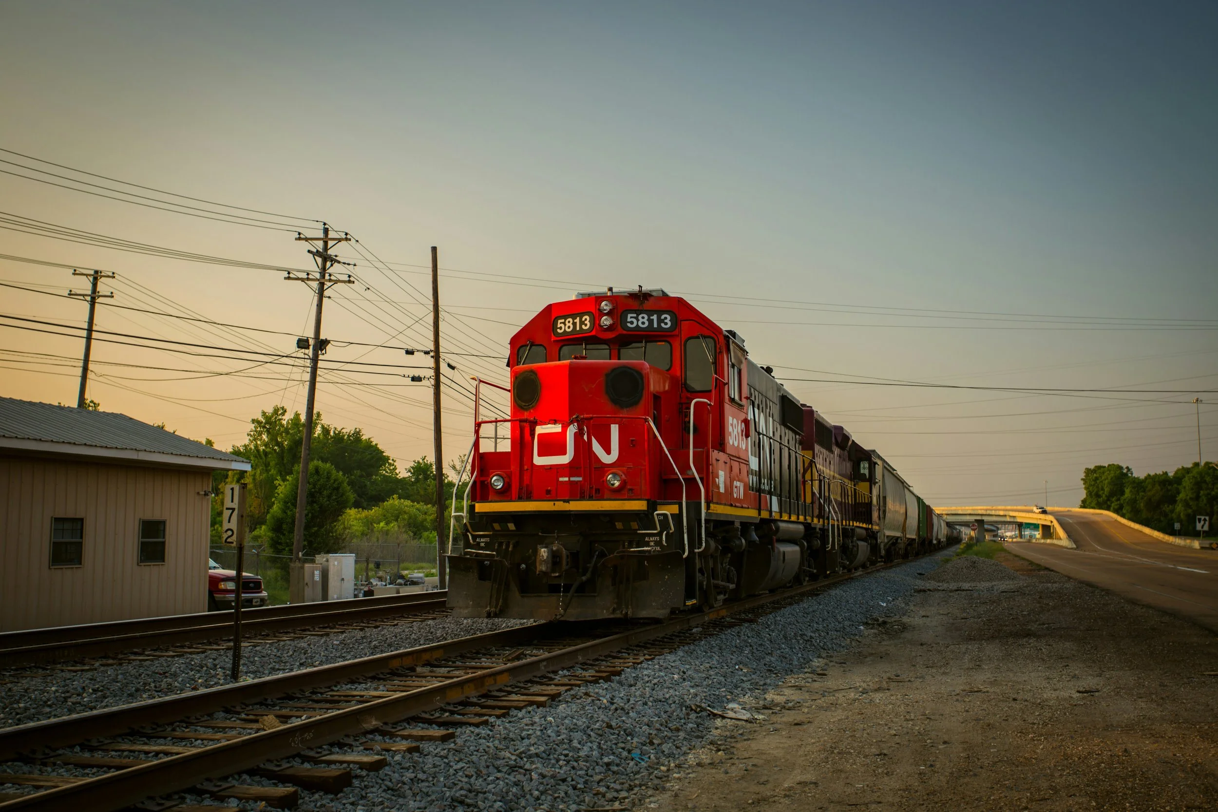 A red train engine numbered 5813 on railway tracks at sunset with power lines and trees in the background.