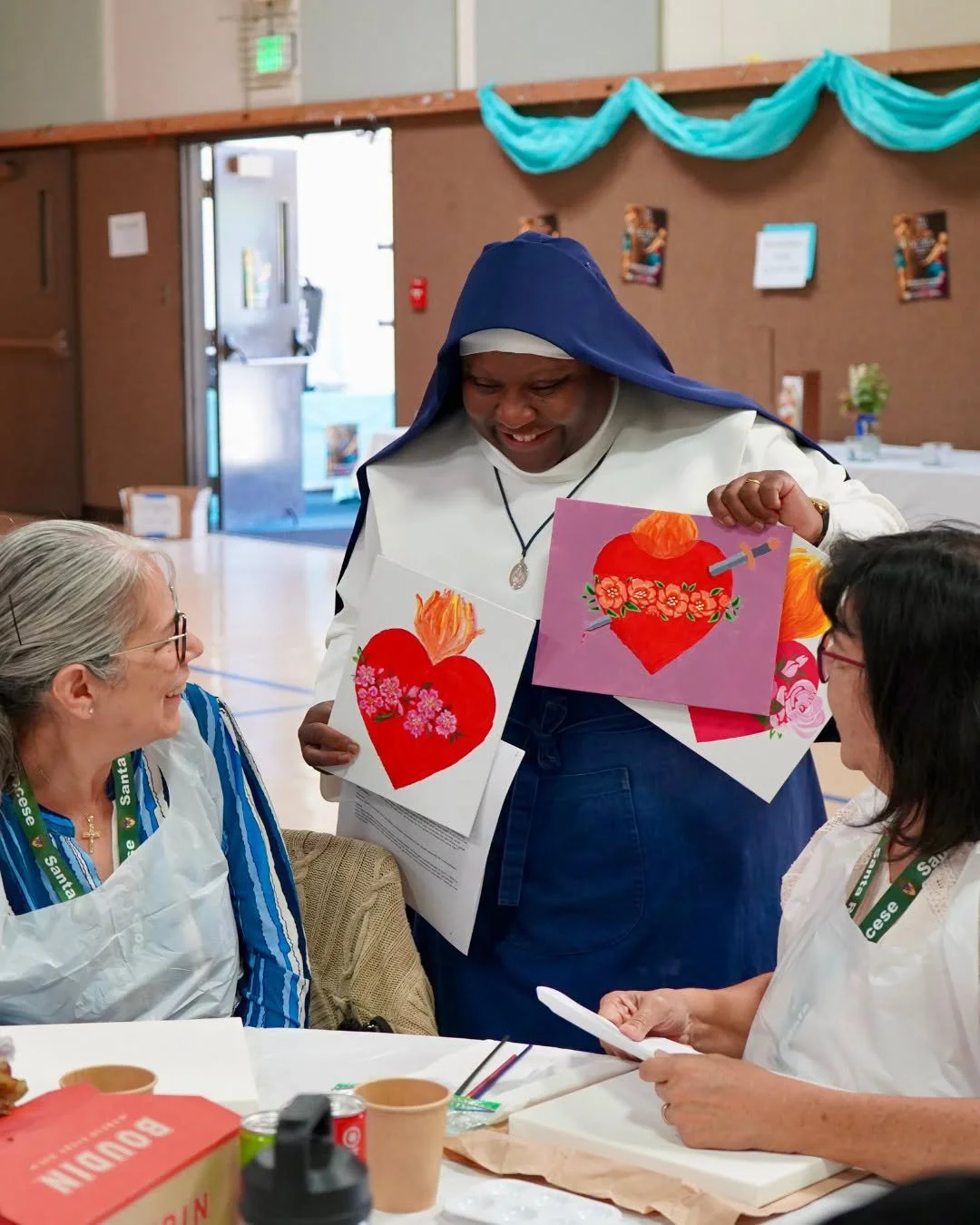 A Marian Sister of Santa Rosa showing artwork to two ladies at a women's conference at the Cathedral