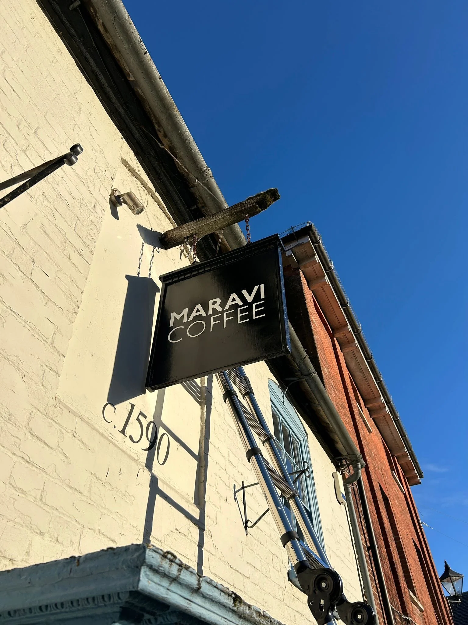 Sign renovation for Maravi Coffee. Repainting an existing sign and hand painting their logo font on top, double sided.